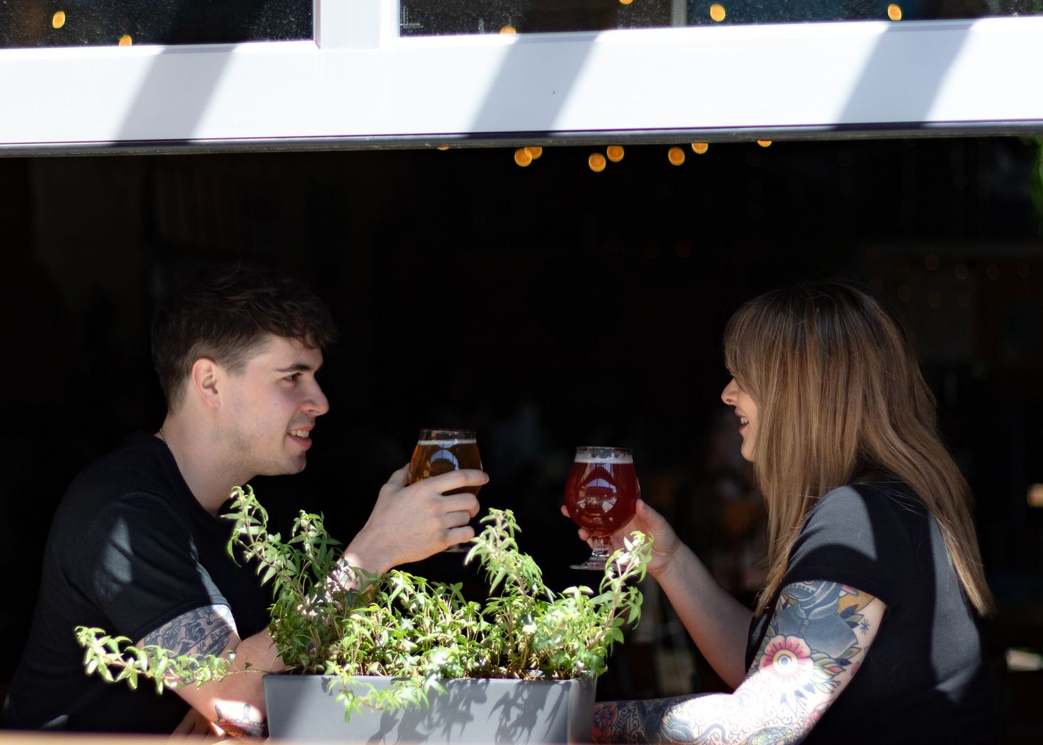 Silhouettes of people sitting at a dimly lit bar with cocktails and string lights in the background.