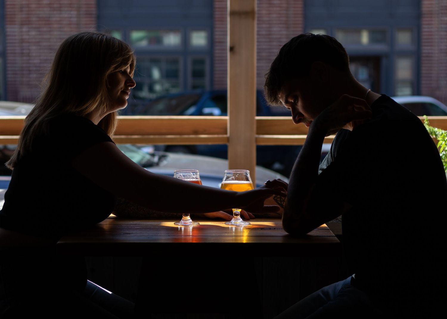 Bar interior with dark silhouettes against window and brick wall backdrop.