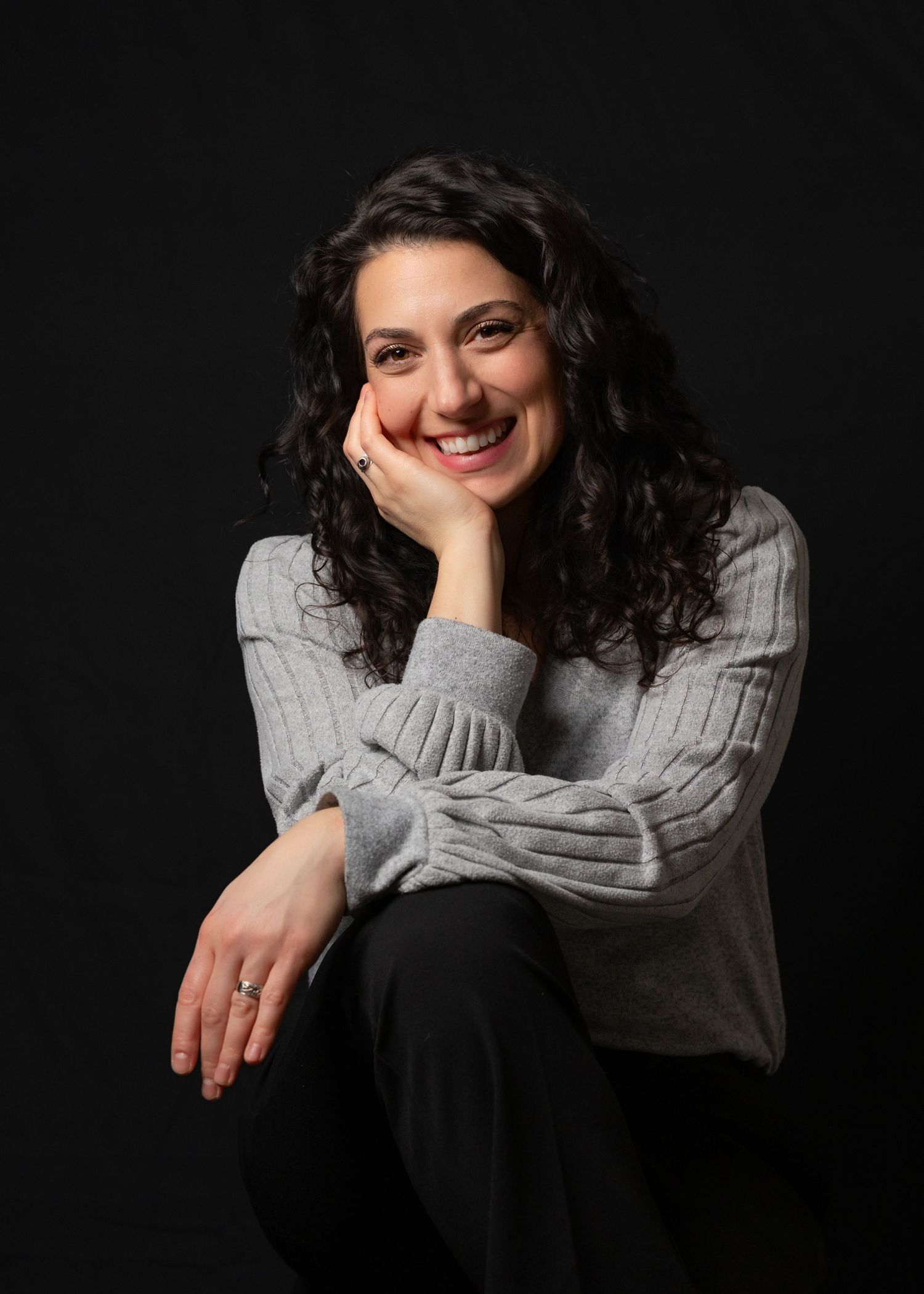 Person in gray sweater and black pants sitting against dark background showing different expressive poses.