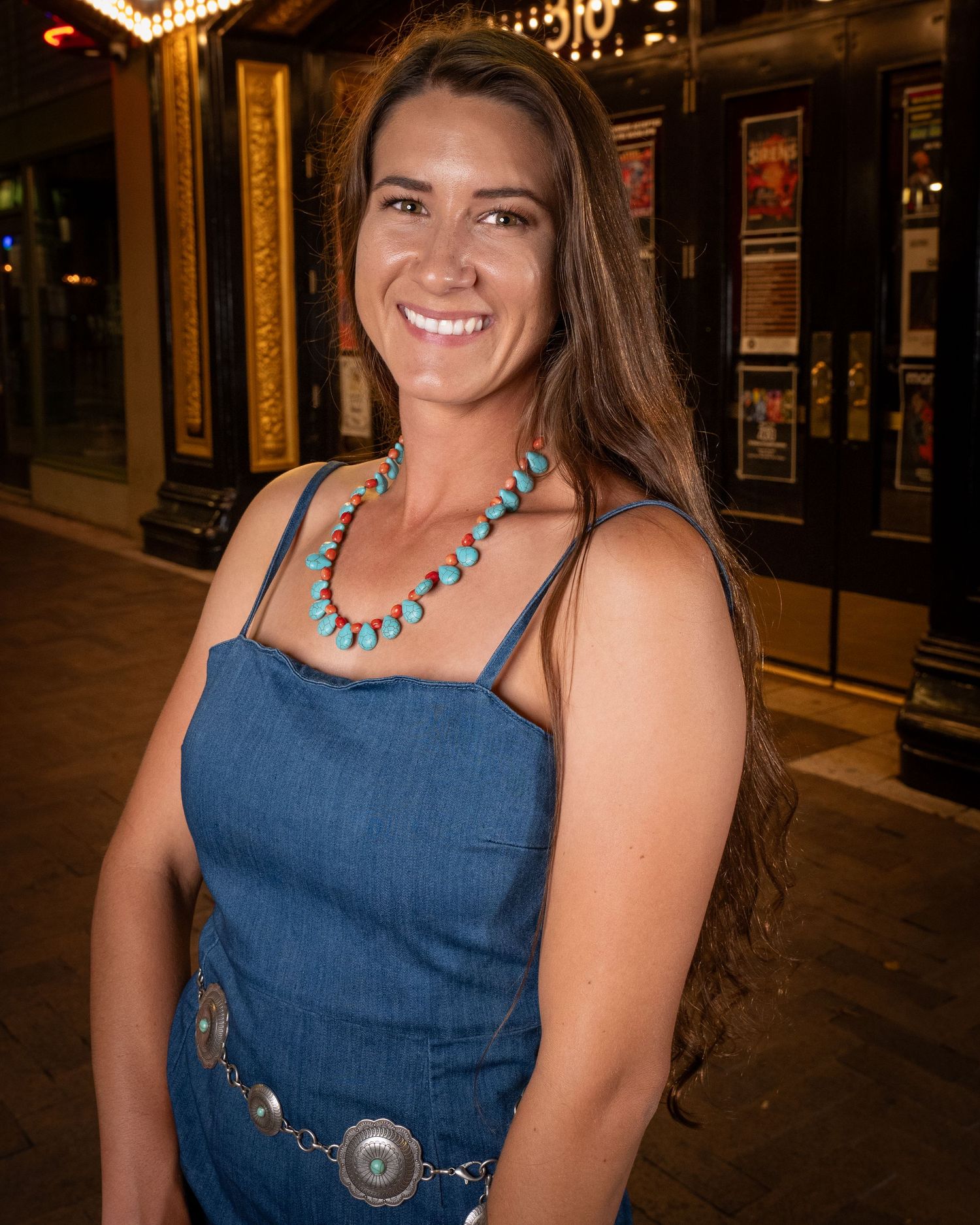 Portrait of a woman in denim dress with turquoise necklace outside at night.