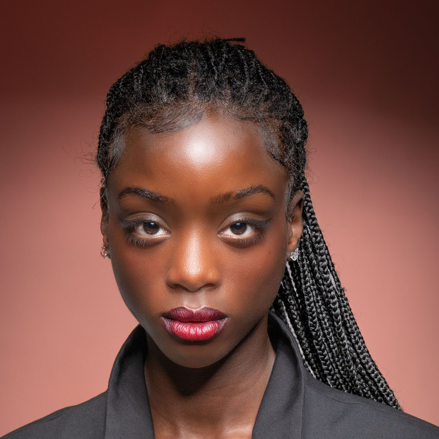 Professional beauty portrait with braided hair and bold red lipstick against warm background.