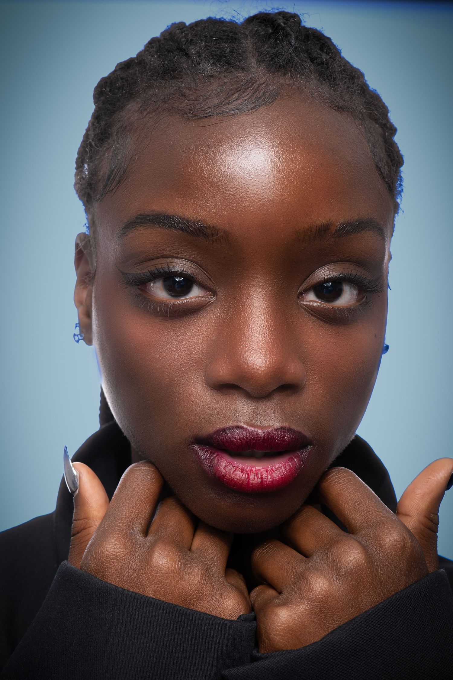 Close-up beauty portrait showcasing flawless skin and burgundy lipstick against blue backdrop.