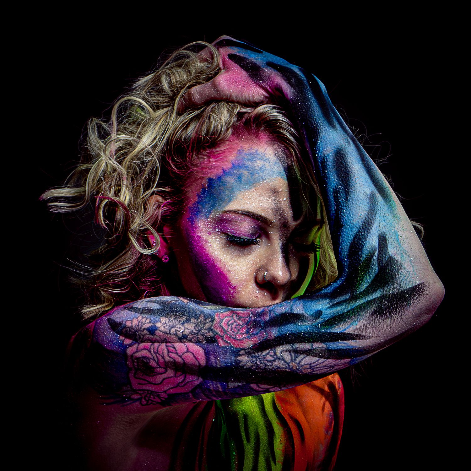 Artistic portrait with neon body paint and fabric creating a colorful abstract composition.