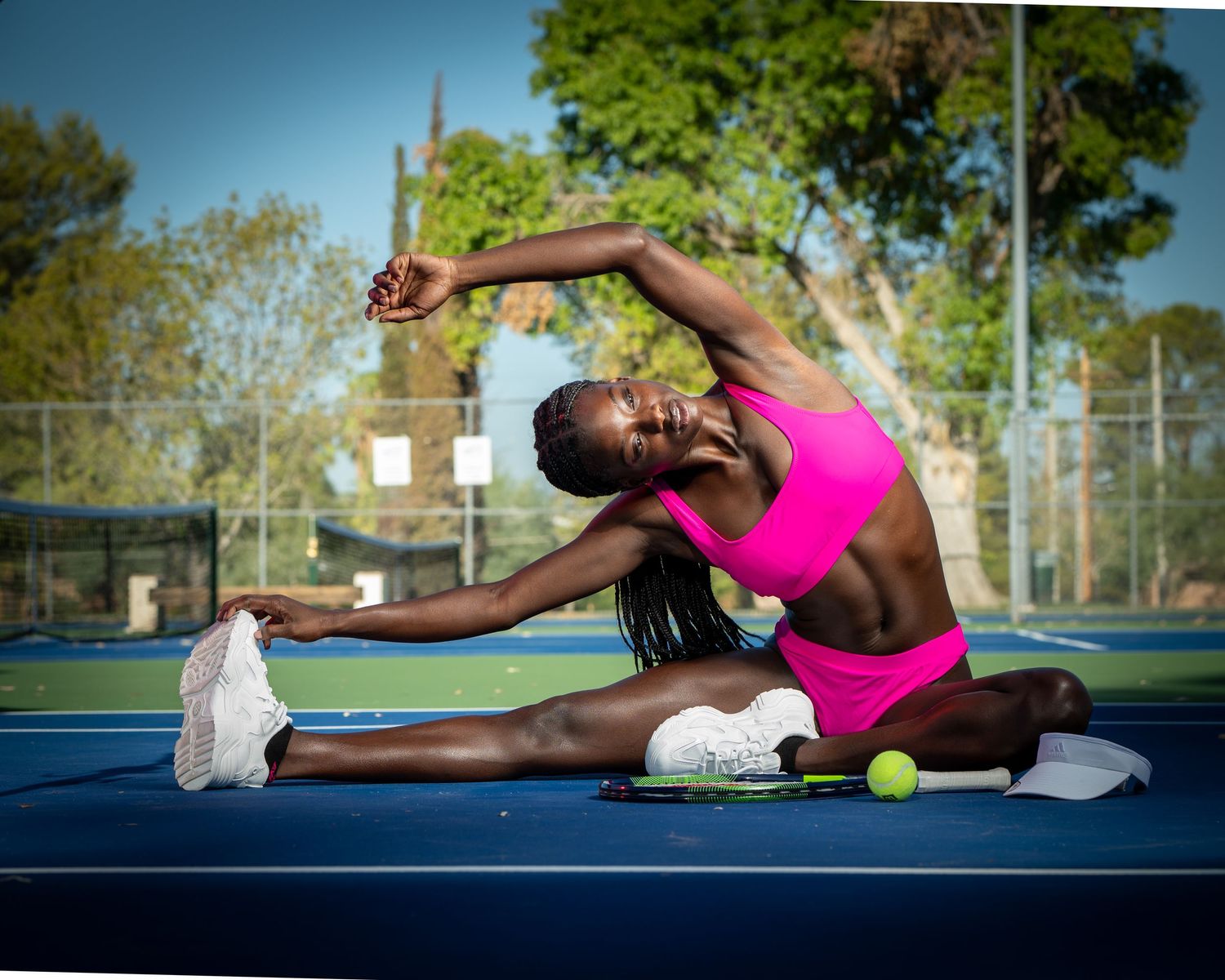 Athlete in pink sportswear performs a deep forward stretch on an outdoor athletic court during training.