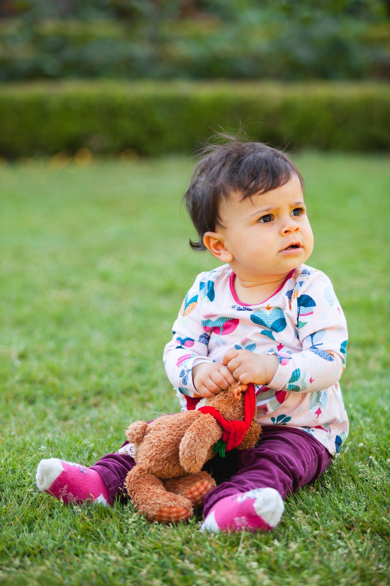 Bébé assis dans l'herbe, l'air interrogatif, une peluche à la main