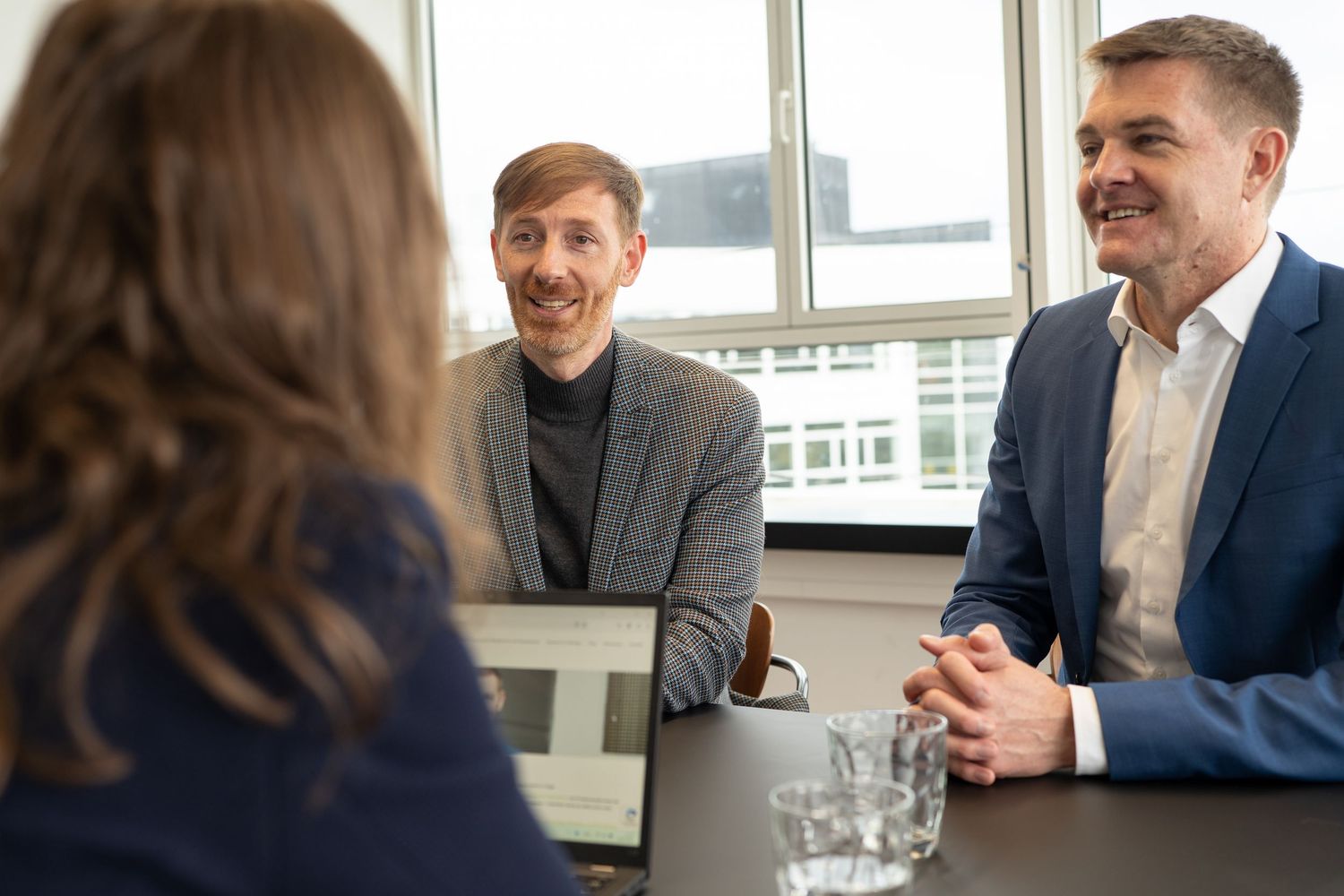 Business meeting scene in modern office with natural lighting through large windows.