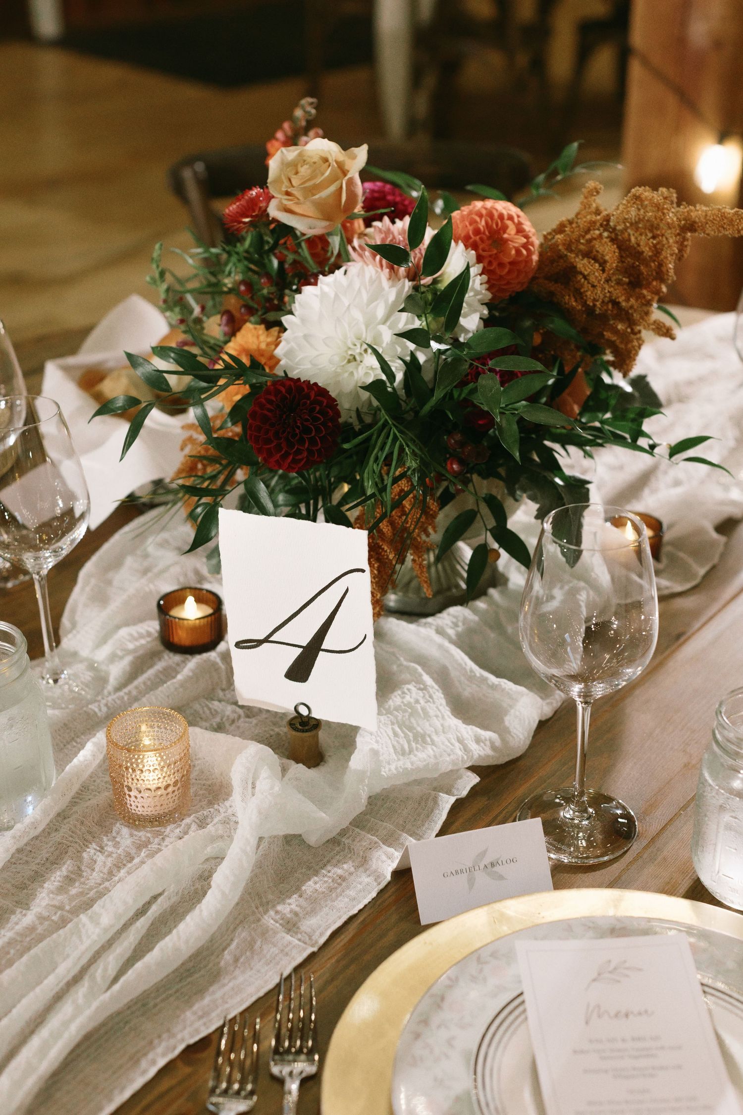 Crystal chandeliers hang from exposed wooden barn beams with string lights creating elegant atmosphere.