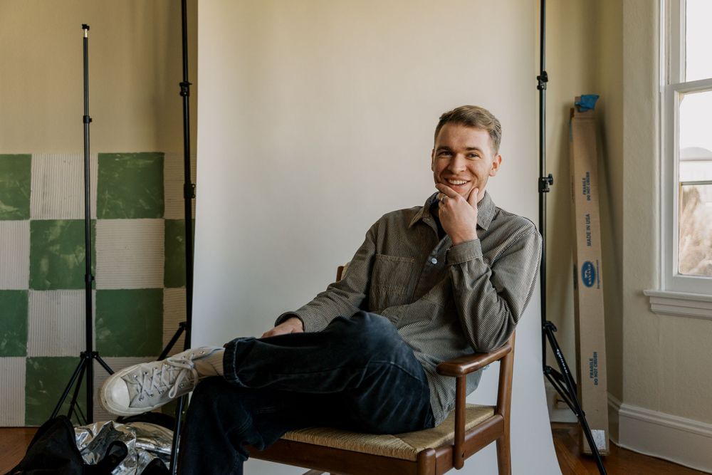 Person relaxing in a chair against checkered green and white tiled wall in a bright indoor space.