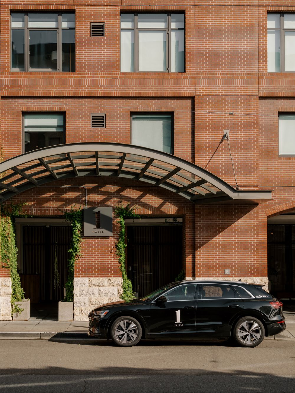 A black luxury SUV parked under a curved glass awning entrance of a modern brick apartment building.