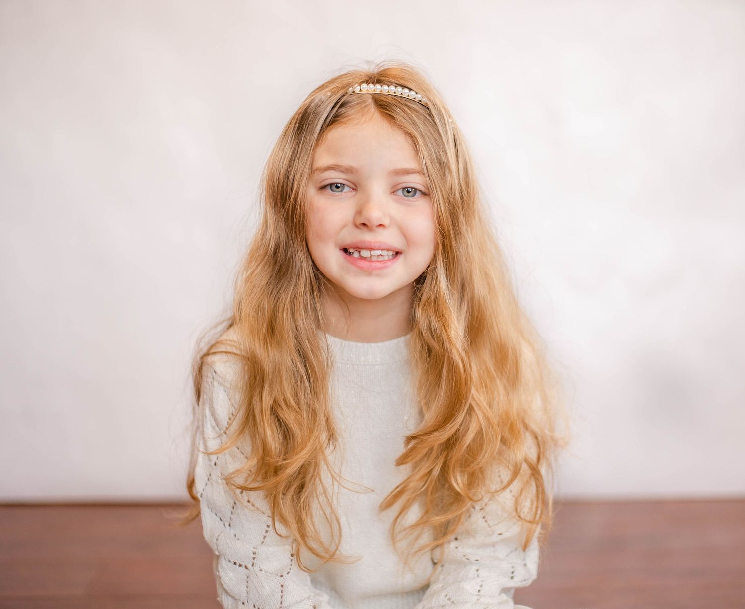 Portrait of person wearing white sweater against neutral background with flowing blonde hair.