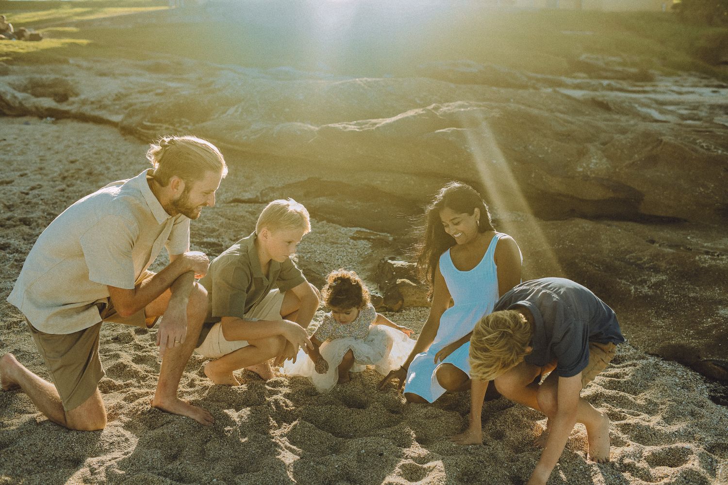A family gathered on the sandy beach at Cronulla, digging and playing in the sand together under the warm sunlight.