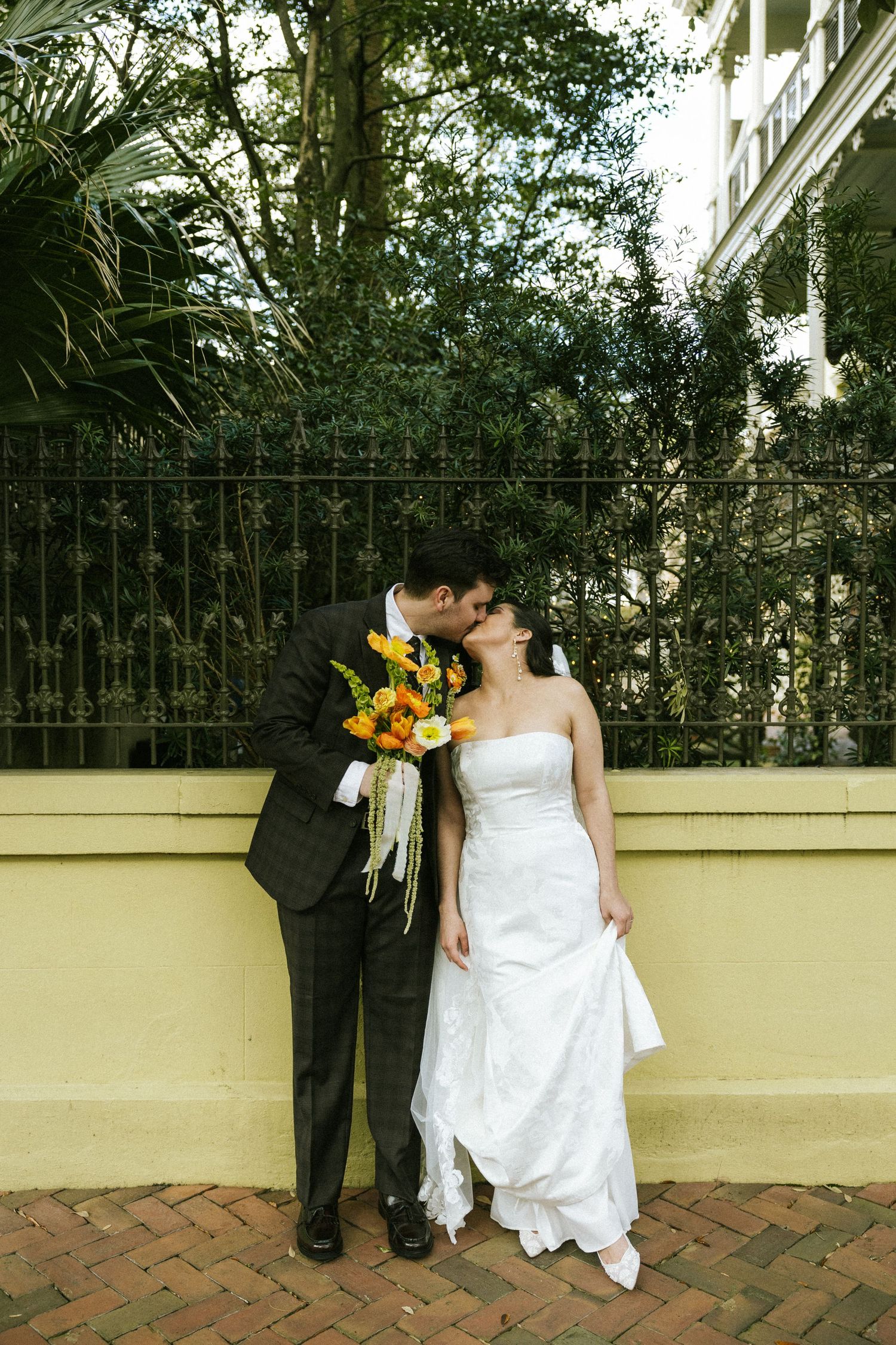 A couple stands cuddled up under the bride's veil on Gaston Street, holding a warmly-colored bouquet