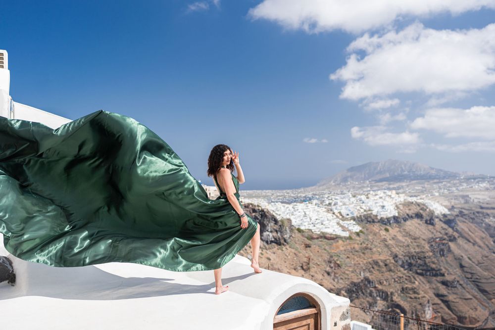 Emerald green dress fabric flows in the wind against Santorini's white architecture and coastline.