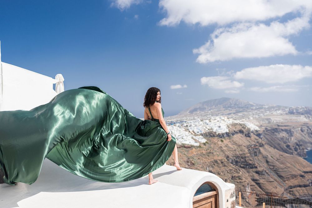 Forest green silk fabric billows dramatically on a white rooftop overlooking Santorini's landscape.
