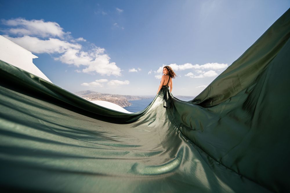 Dramatic waves of emerald fabric create dynamic shapes against a blue sky in Santorini.