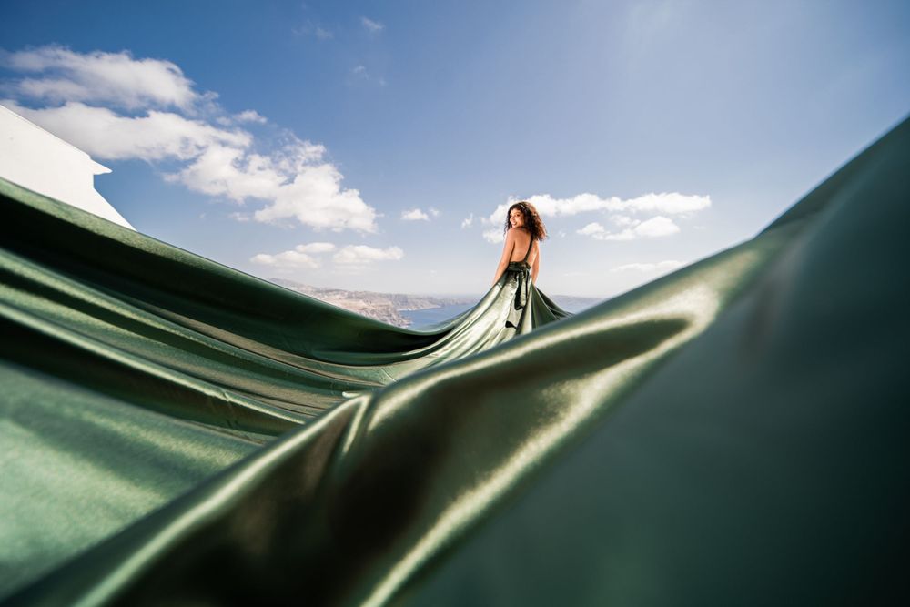 Green flowing fabric creates rolling waves against bright blue skies in Greece.