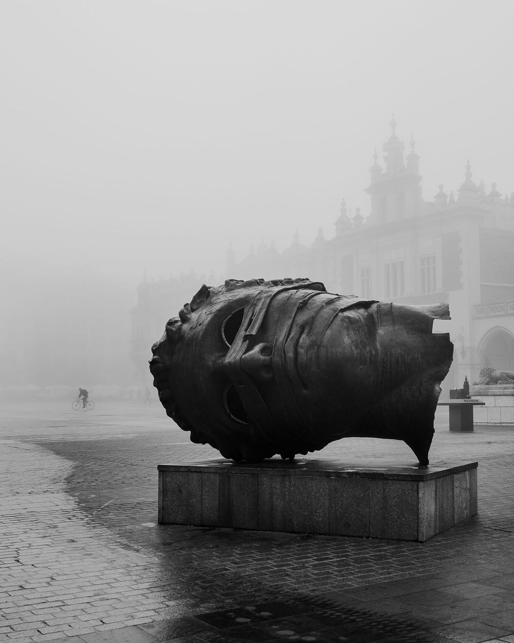 Large sculptural monument lying horizontal in foggy town square.