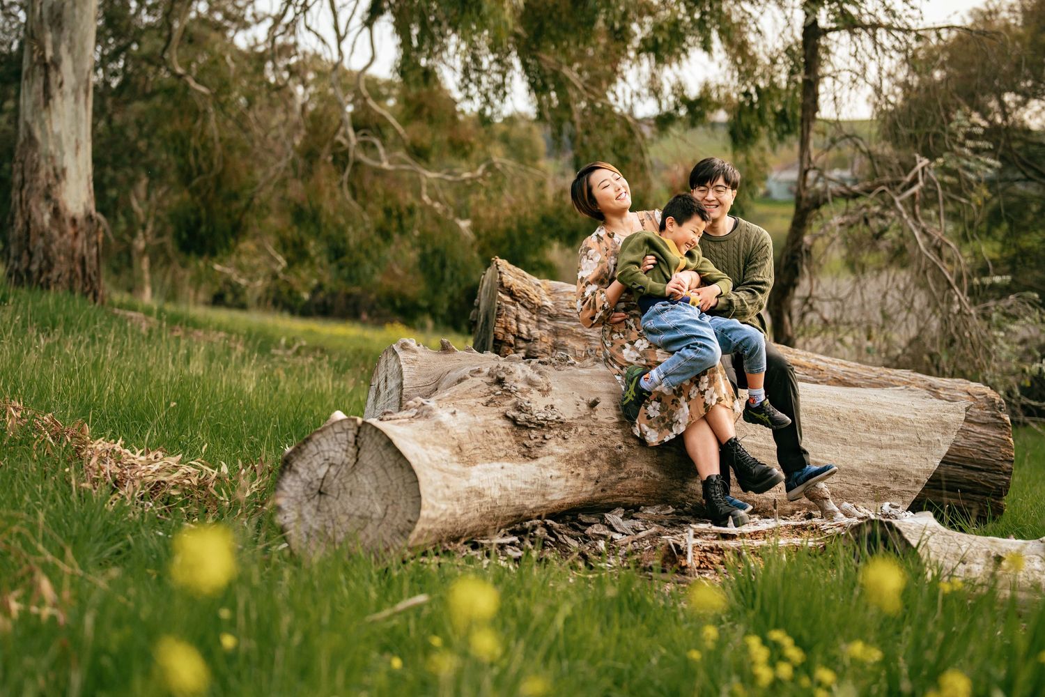 Two children sit together reading on a large fallen log surrounded by greenery and wildflowers.