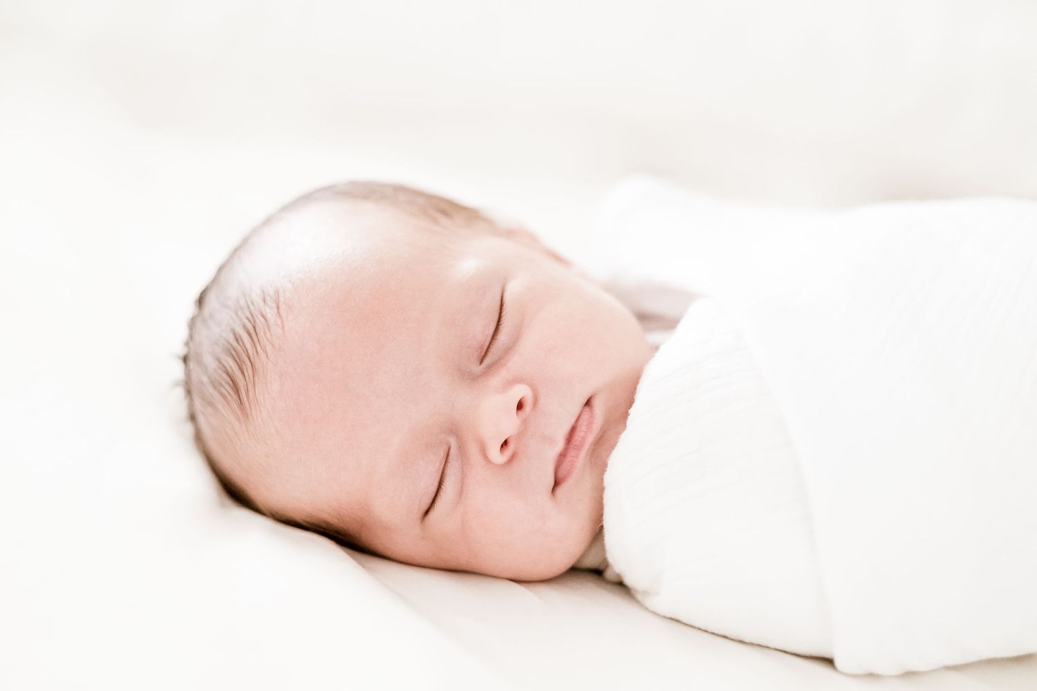 A series of peaceful black and white portraits of a sleeping newborn wrapped in white fabric.