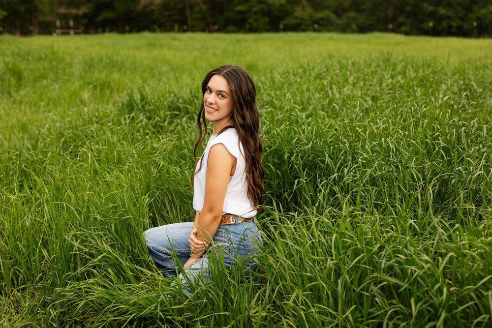 Senior graduate outdoor portrait in tall green grass field.