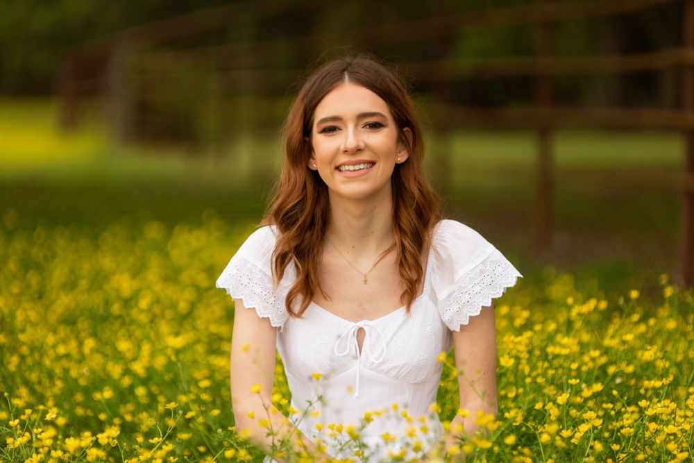 Senior graduate portrait in a field of yellow wildflowers on a sunny spring day.