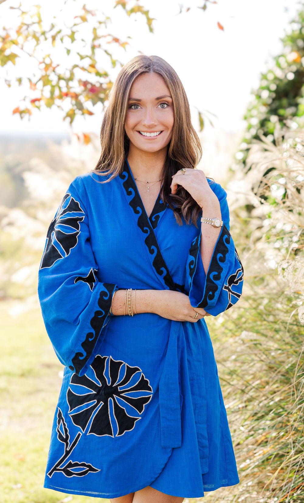 Woman in bright blue embroidered dress with balloon sleeves poses against autumn foliage.