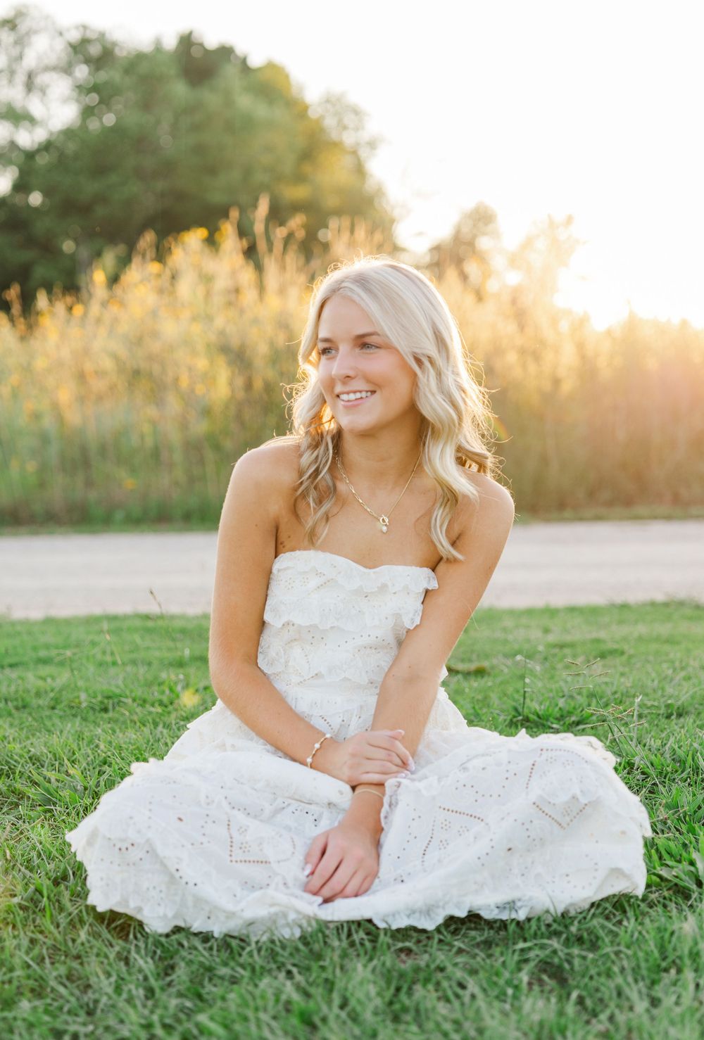 Sunset portrait in white lace dress sitting on grass.