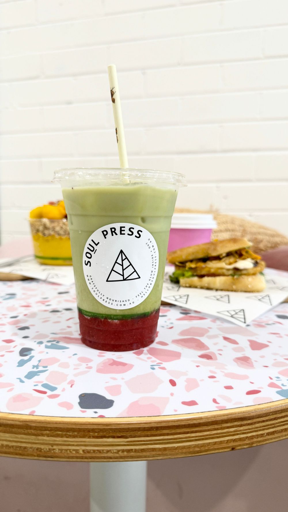 A layered matcha and red fruit drink from Soul Press cafe served on a patterned table with food in background.