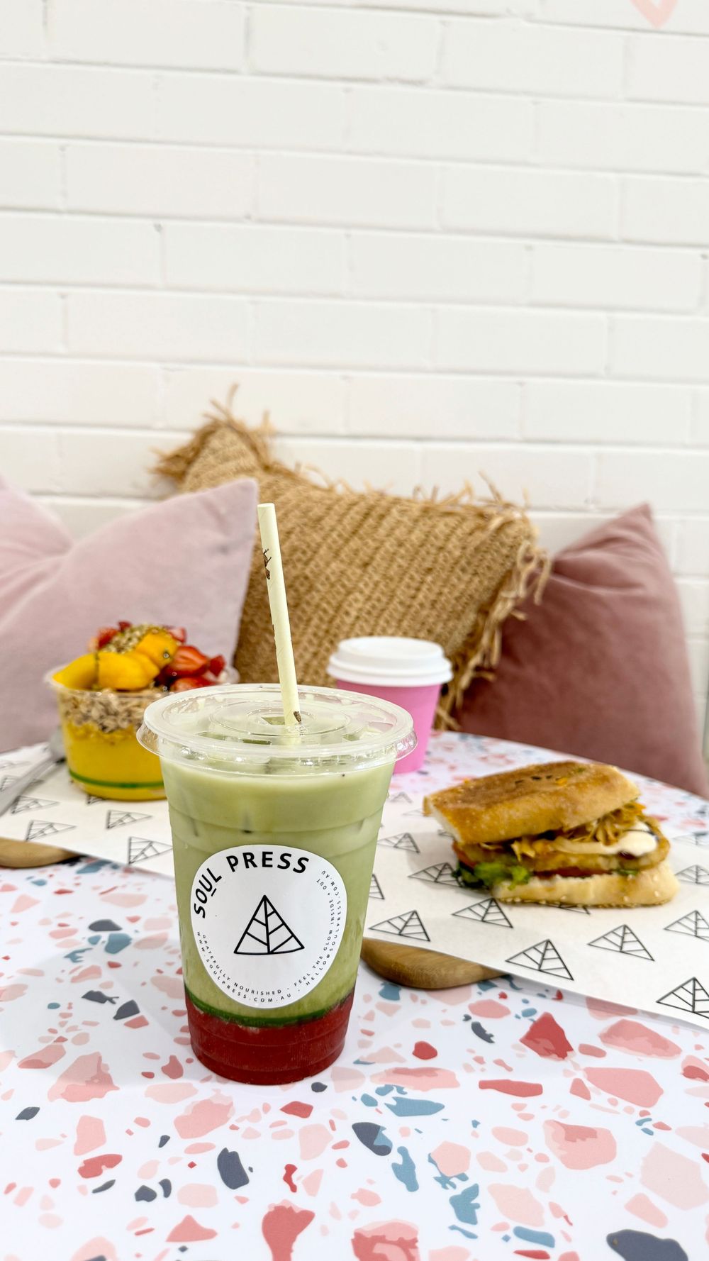 Soul Press green smoothie and sandwich on patterned tablecloth with pink cushions.