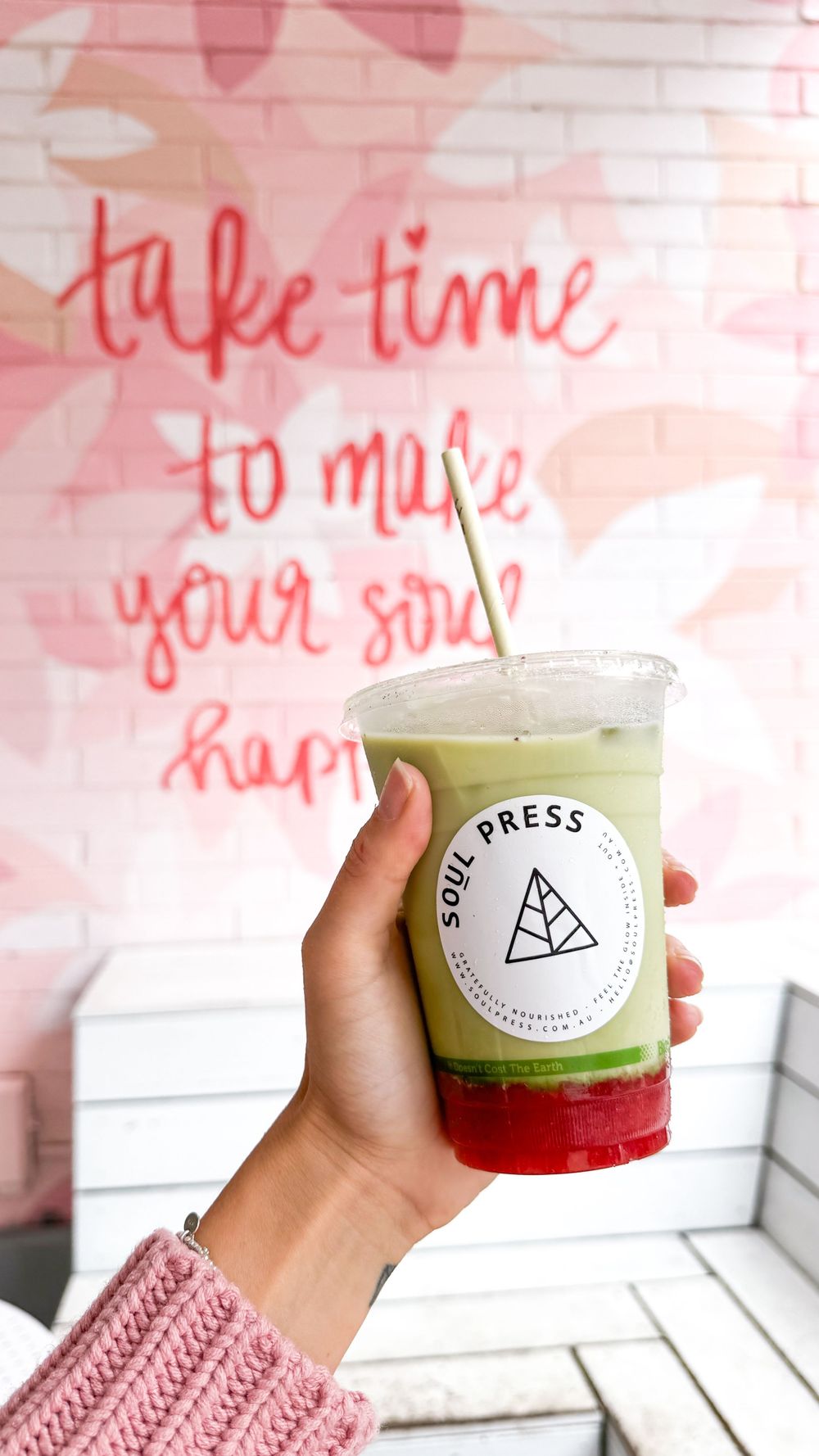 Hand holding layered Soul Press drink against pink wall with inspirational quote.