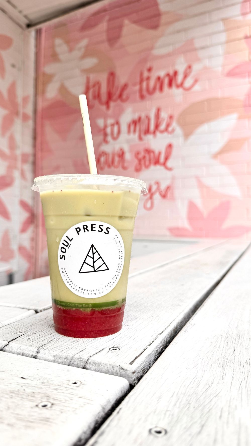 Layered Soul Press smoothie with red base on white wooden bench against pink floral wall.