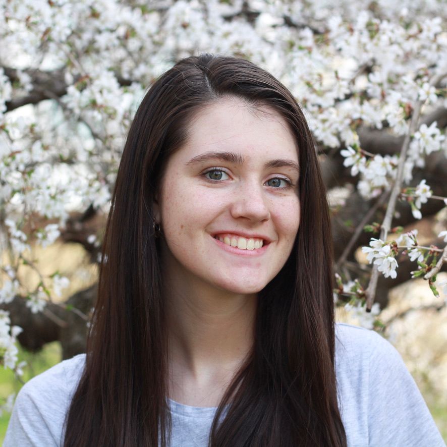 Katie Carr- Young white woman with dark hair in front of flowers