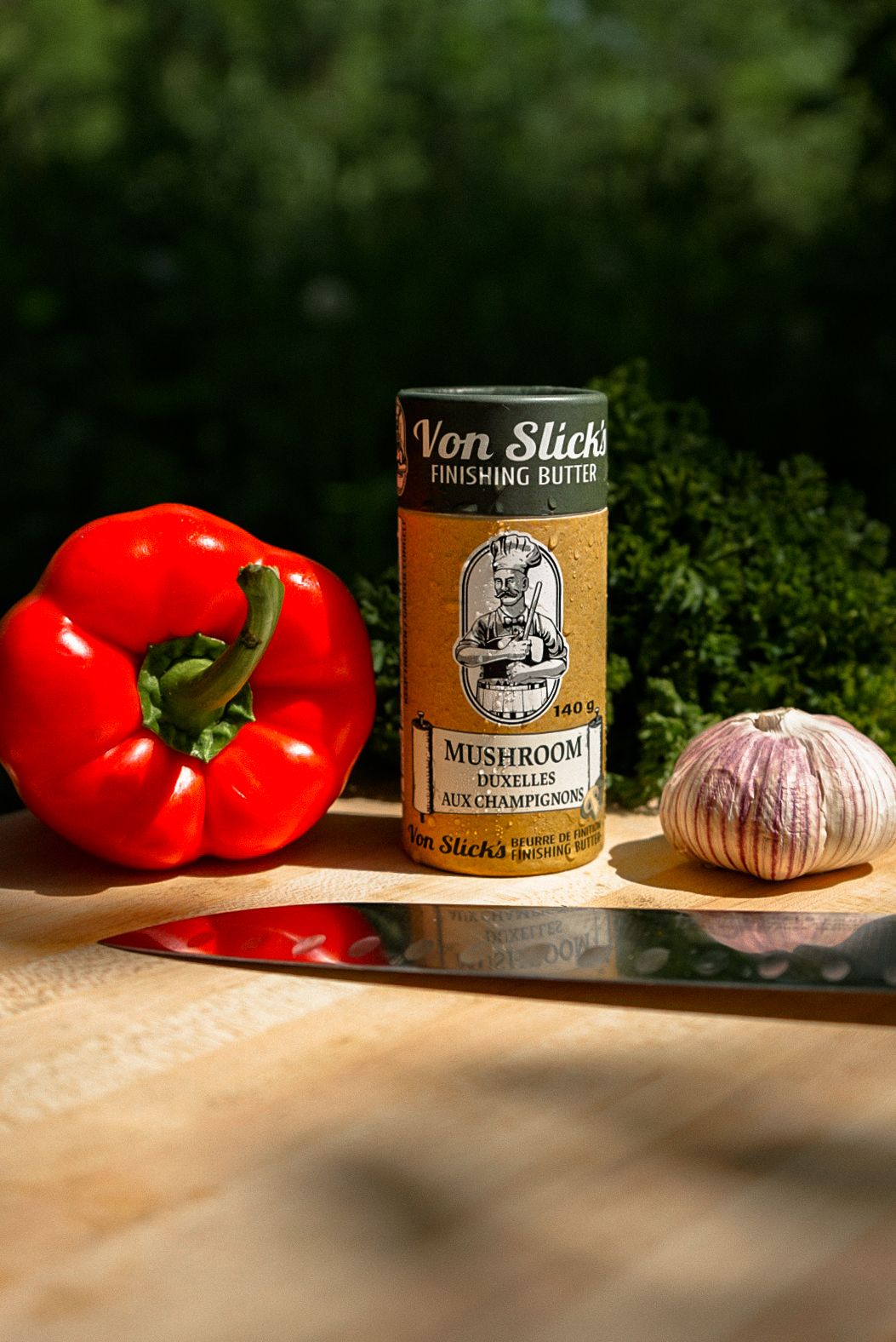 Fresh red bell peppers, garlic, and Von Sticks gourmet butter arranged on a wooden surface.