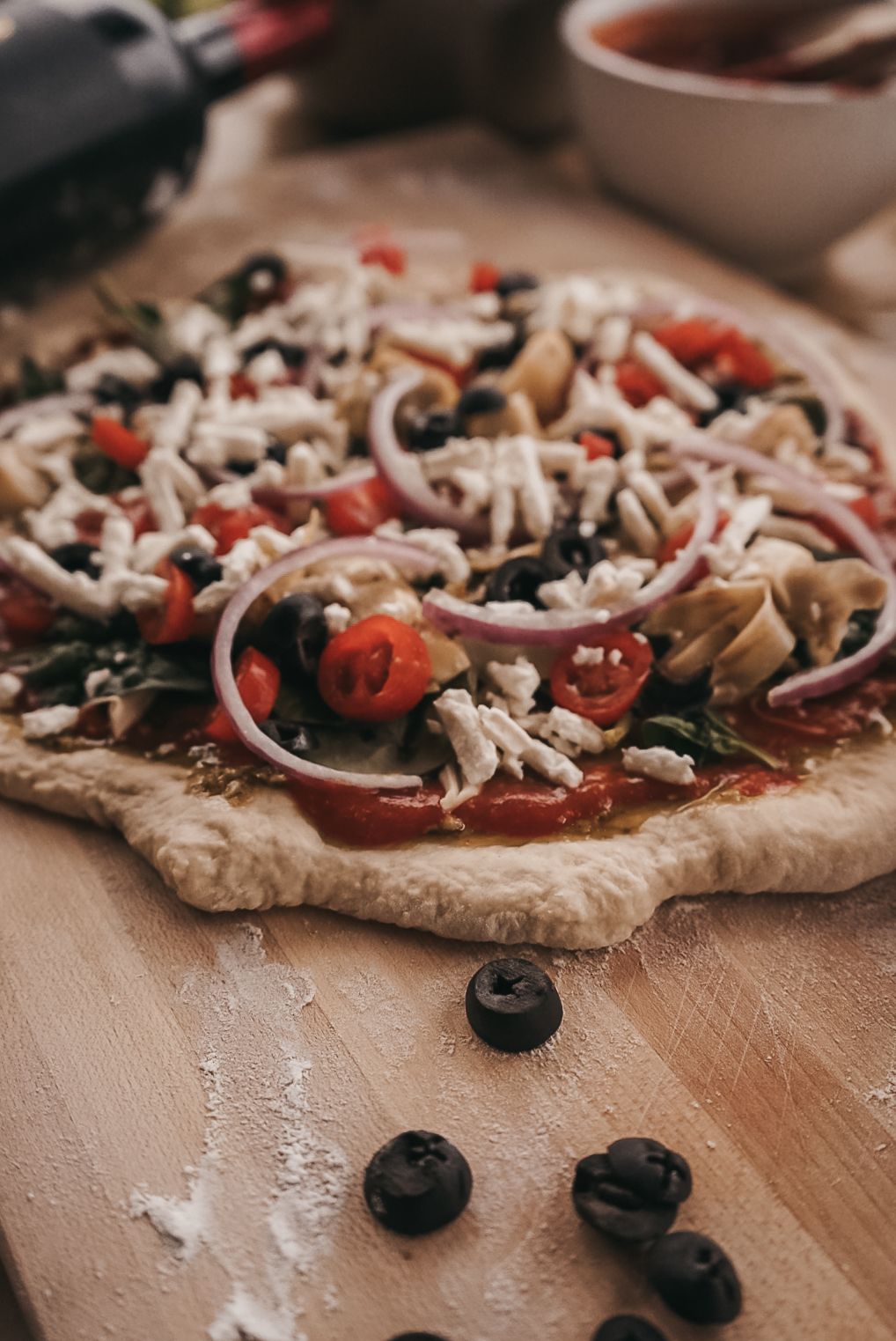 Homemade pizza dough topped with mushrooms, olives, and fresh vegetables.