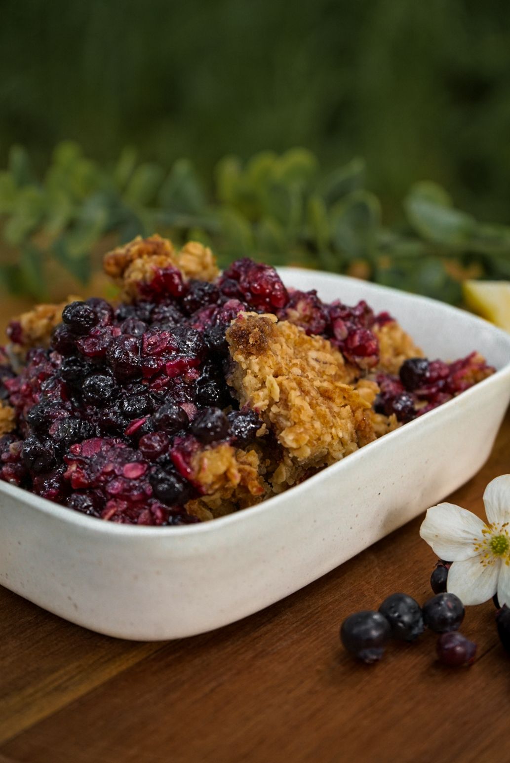 Berry crumble dessert served in white ceramic boat-shaped dishes with fresh flowers.