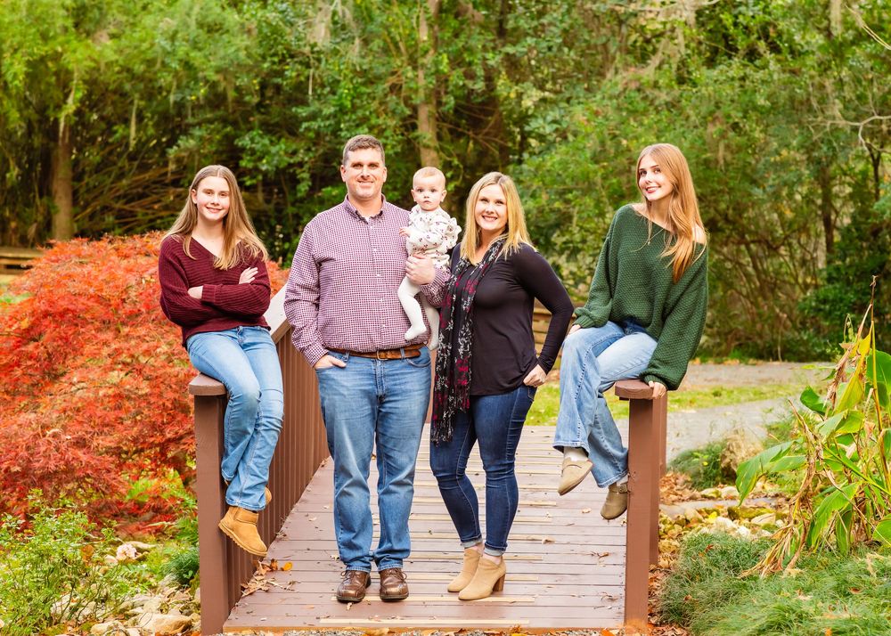A group of people walk together on a wooden boardwalk path through a lush garden setting in autumn.