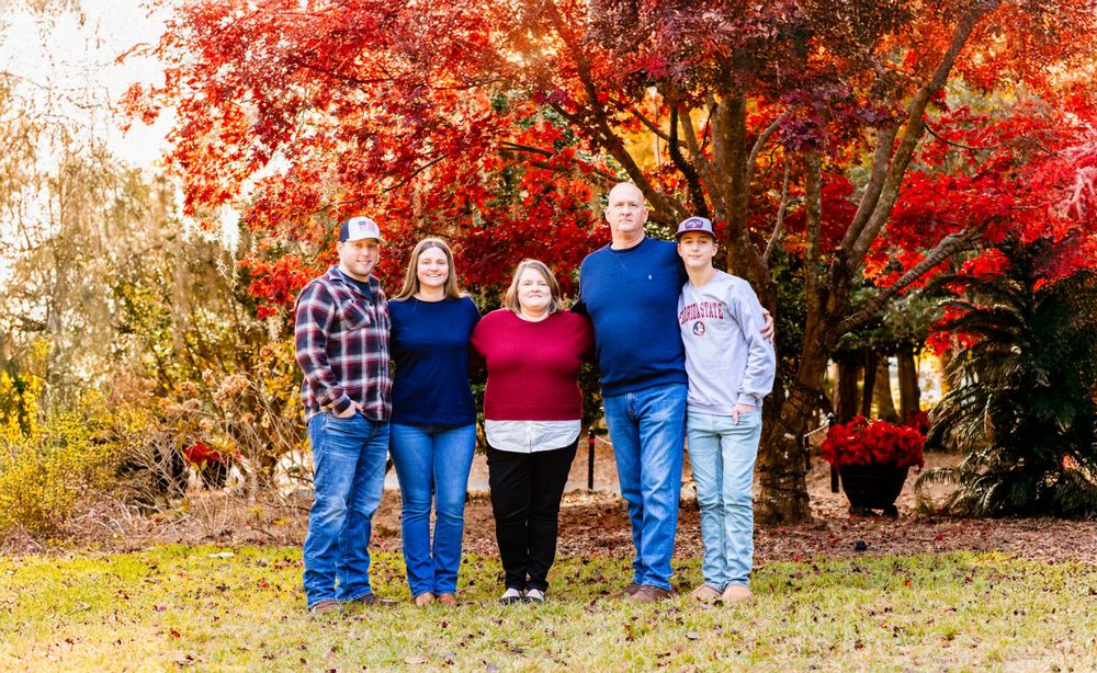 A group stands together under vibrant red autumn maple trees on a bright fall day.