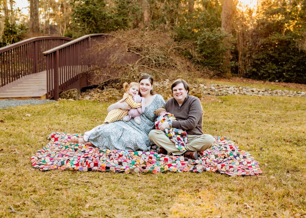 A couple relaxes on a colorful blanket in a grassy field during golden hour sunset.