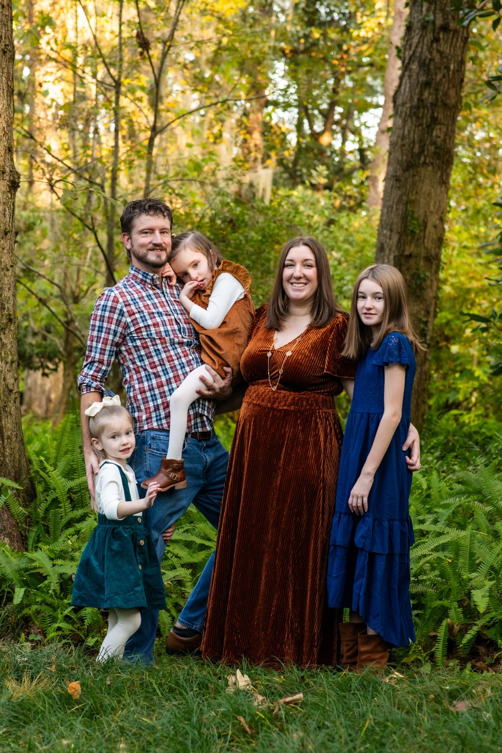 Family poses together in wooded setting wearing coordinated autumn outfits.