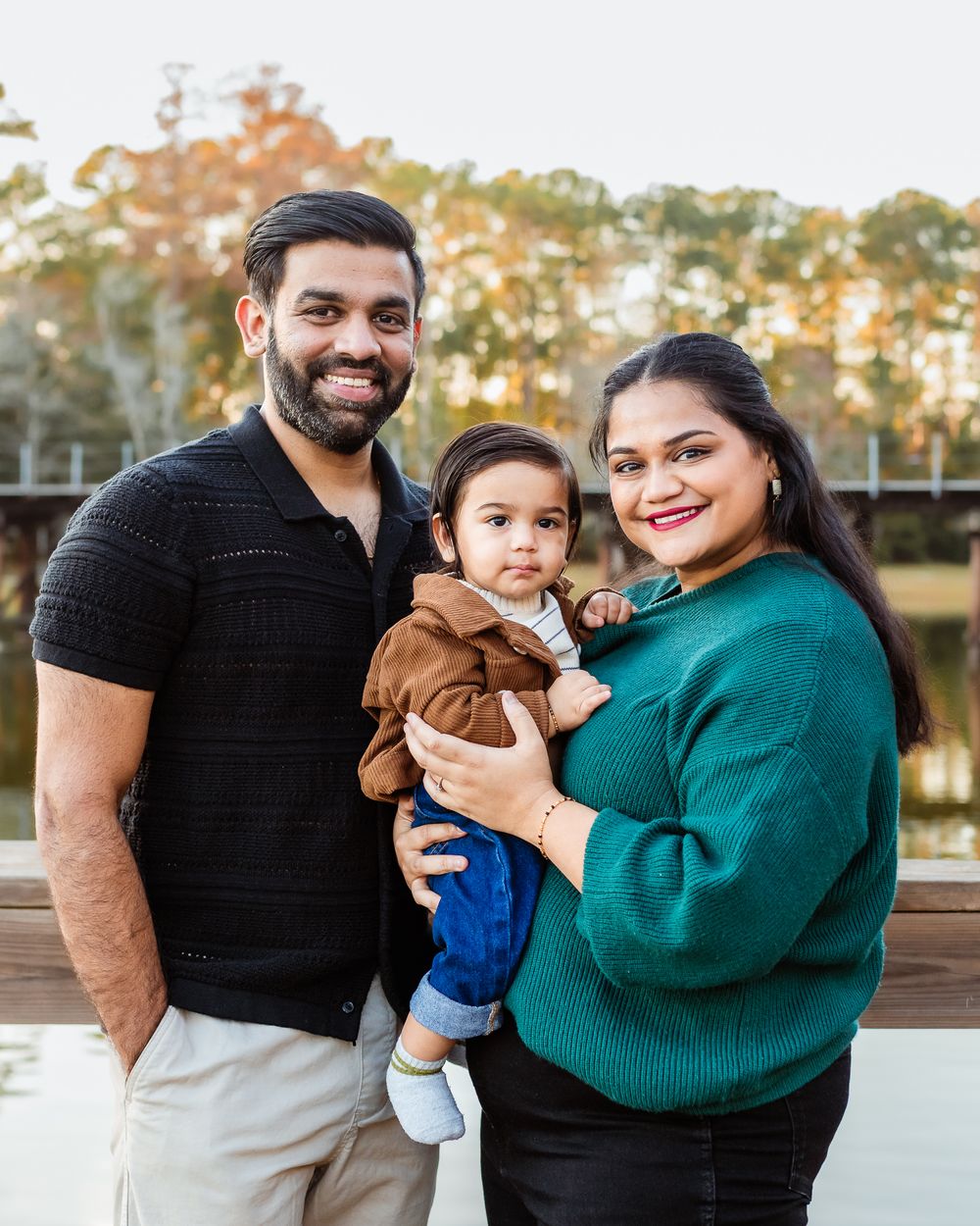Family wearing black and green sweaters poses together outdoors during golden hour.