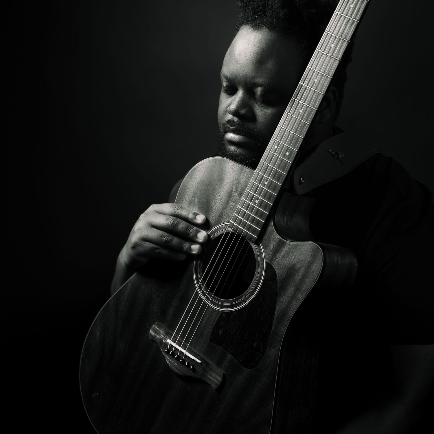 Black and white portrait of musician playing acoustic guitar with dramatic lighting and shadow.