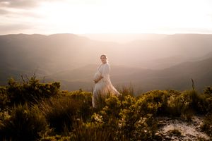 Maternity mama standing on a mountain ridge during golden sunset hour.