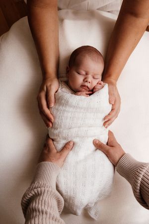 Hands gently swaddling a sleeping newborn in soft white blankets. Captured in a natural light studio in the blue mountains Sydney