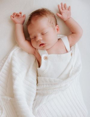Peaceful newborn stretching in white knit blanket against light background. Captured in a natural light studio in the blue mountains Sydney