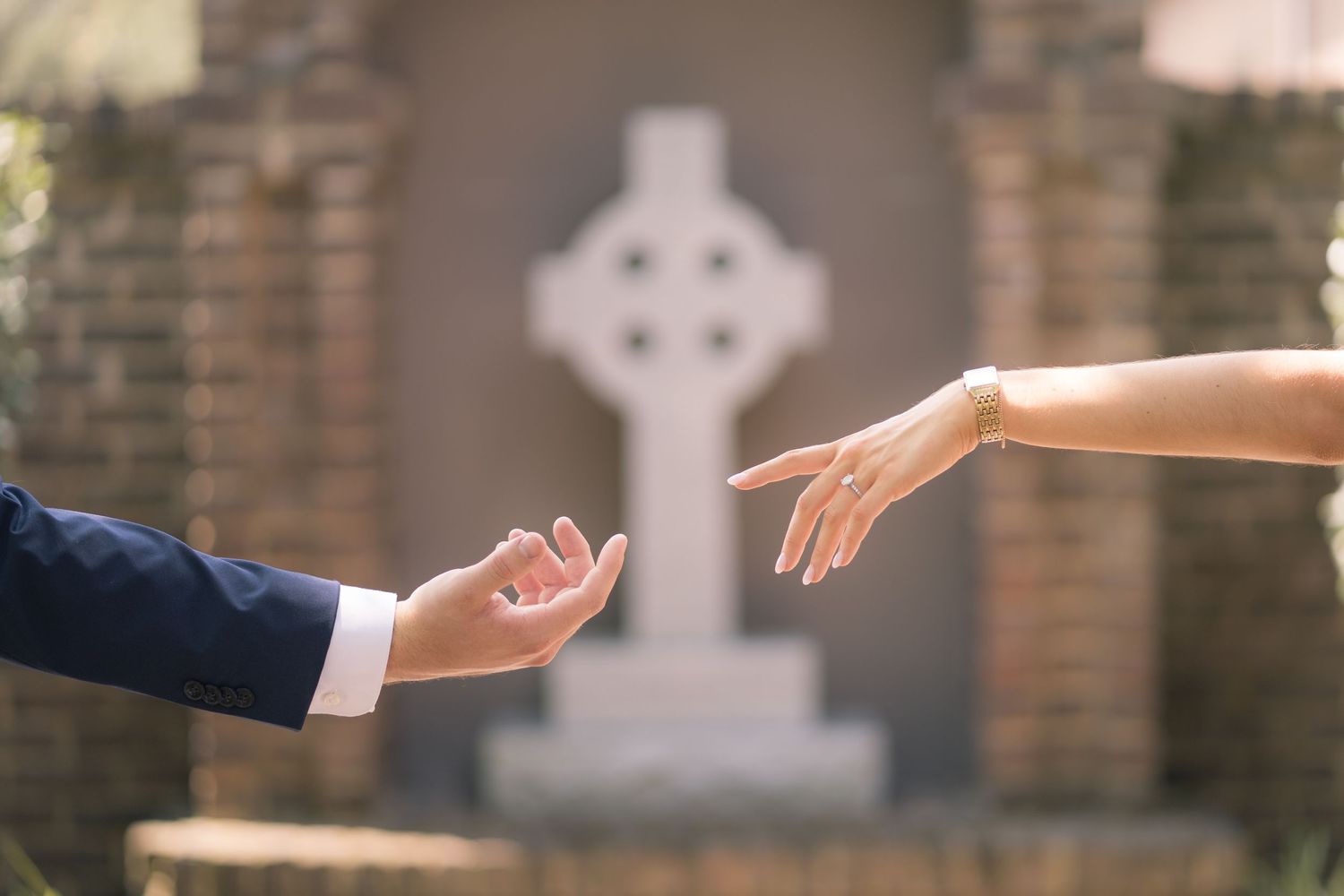 Two hands reaching toward each other with a Celtic cross gravestone in the background.