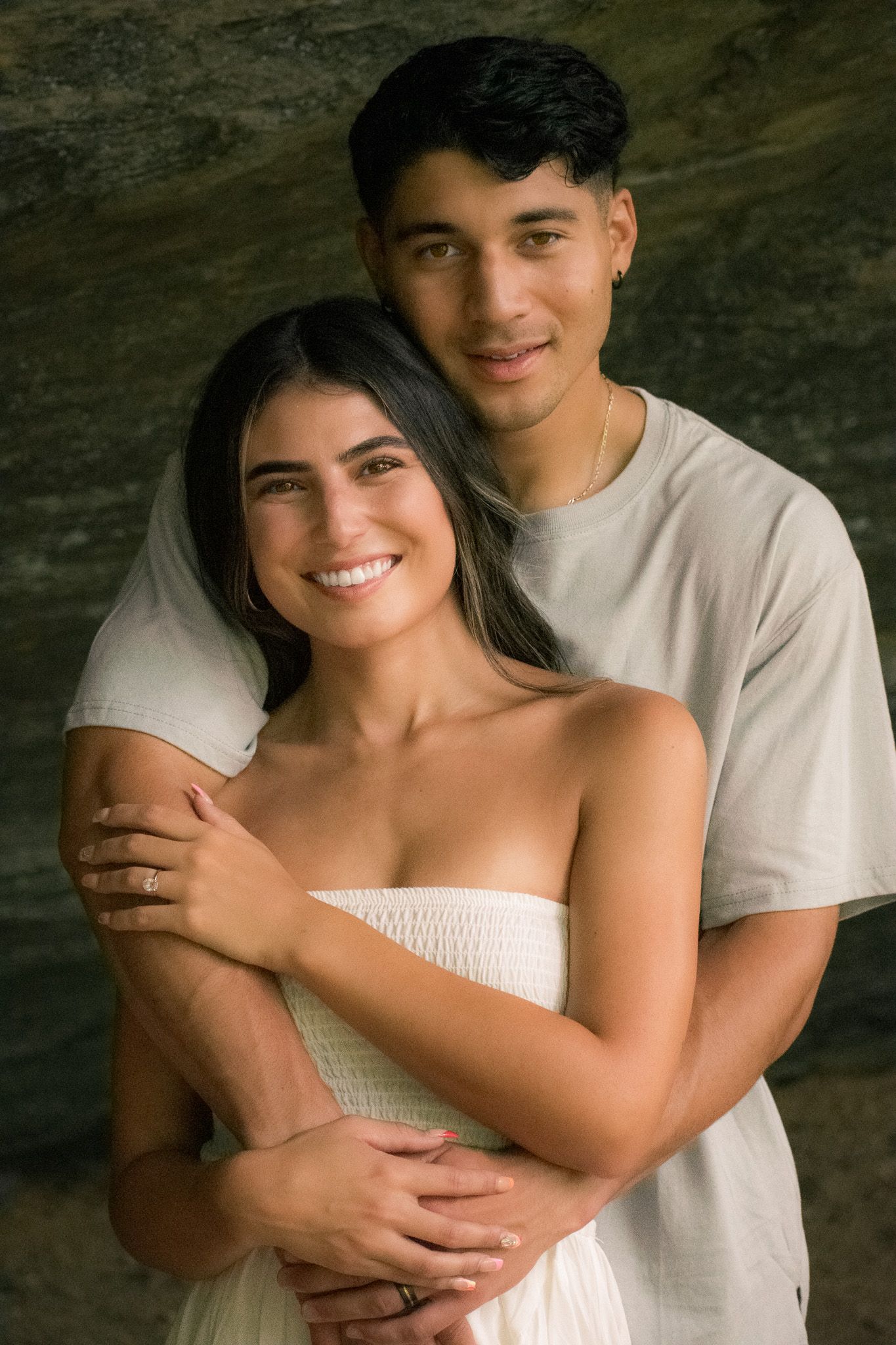 Loving couple embraces while wearing white clothing during indoor photoshoot.