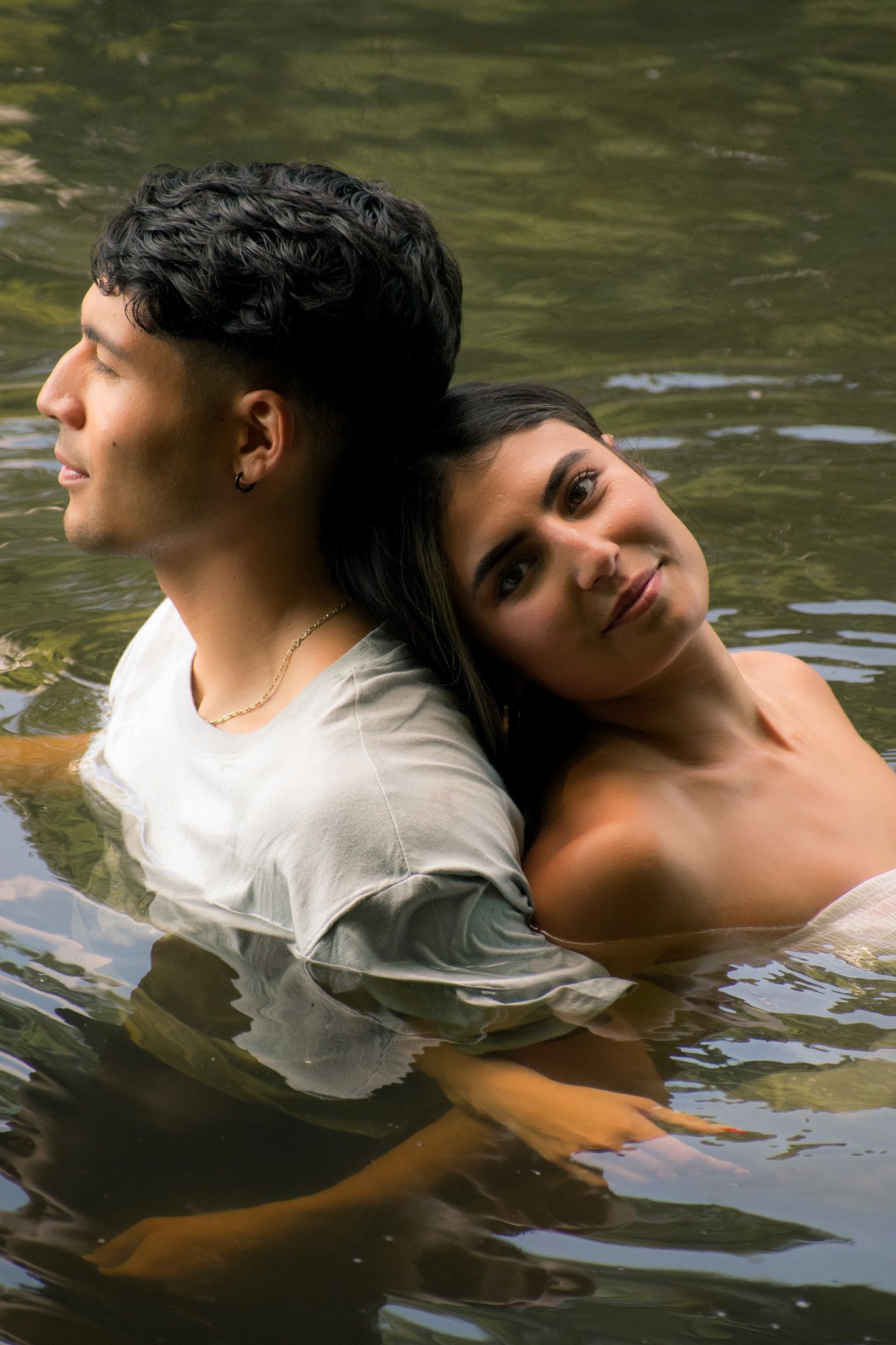 Two people float together in dark water creating artistic ripples.