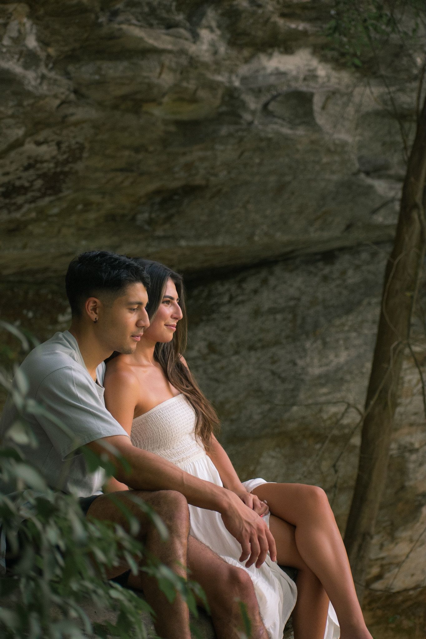 A couple sitting together on rocky terrain surrounded by lush greenery.
