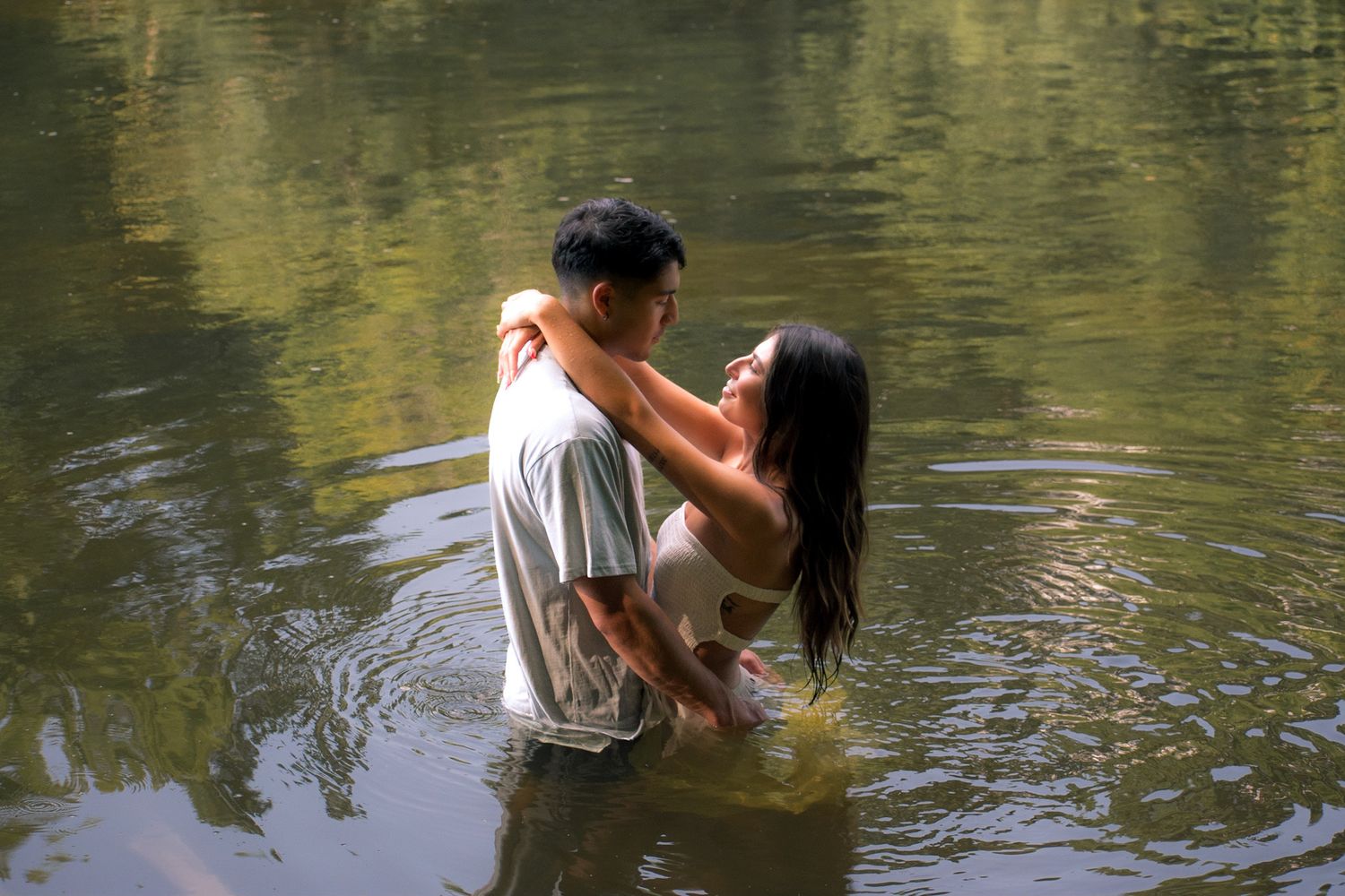 A couple embracing in waist-deep water with forest reflections surrounding them.