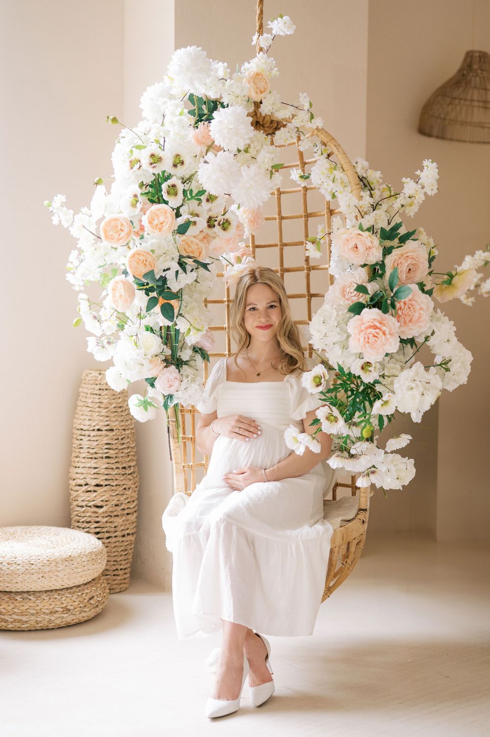 A series of light and airy maternity photos with white flowers, peach roses and woven baskets in a minimalist studio setting.